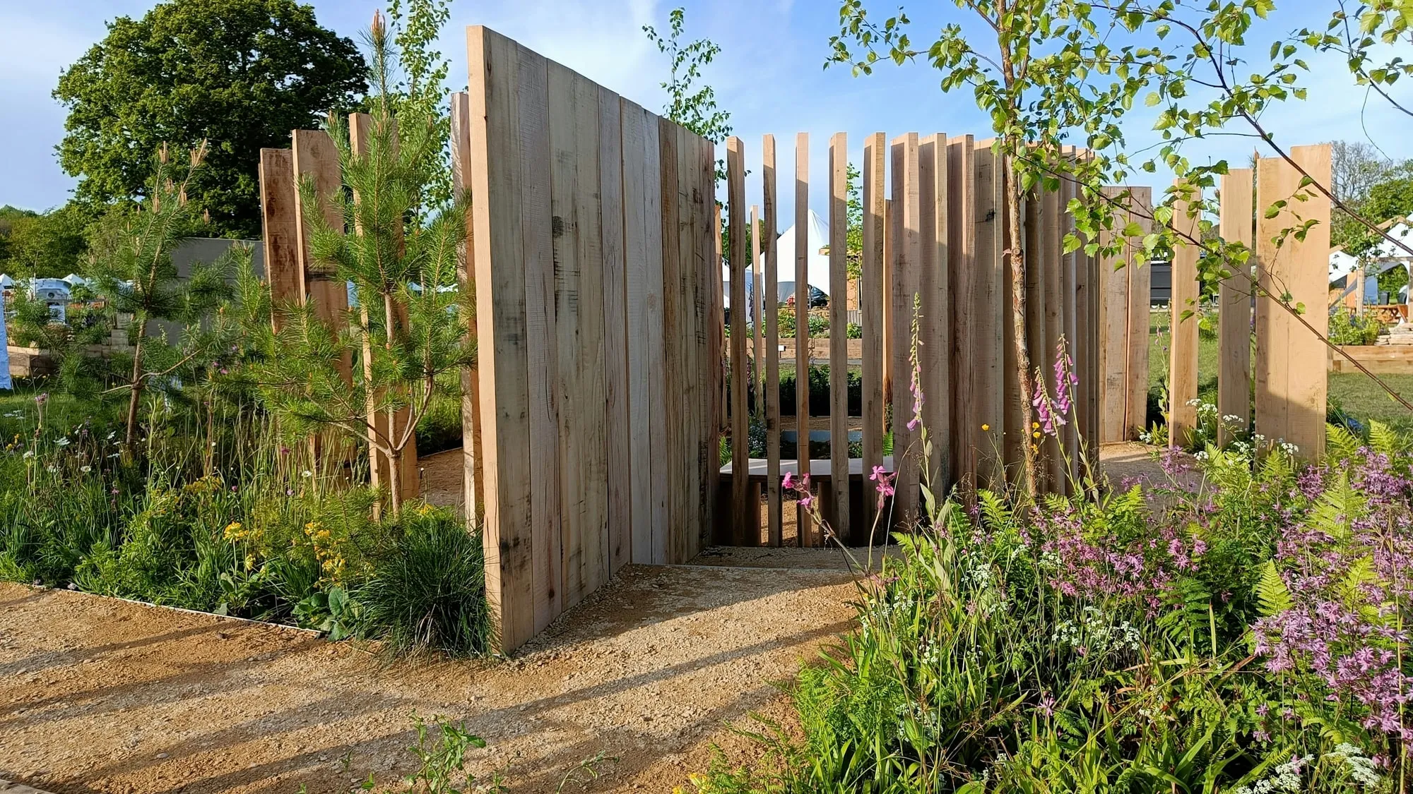 The show garden at the BBC Gardeners' World Spring Fair, vertical oak posts and mixed planting either side of a gravel path