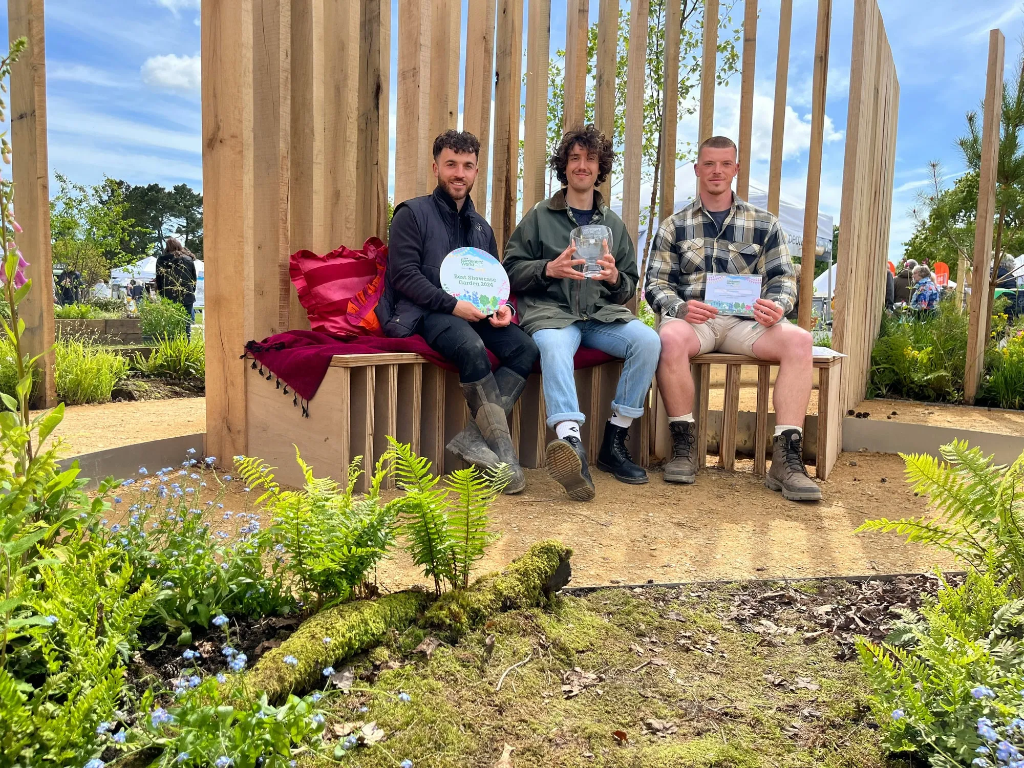 Three of the Your Gardens team sitting on a bench in the show garden with their awards