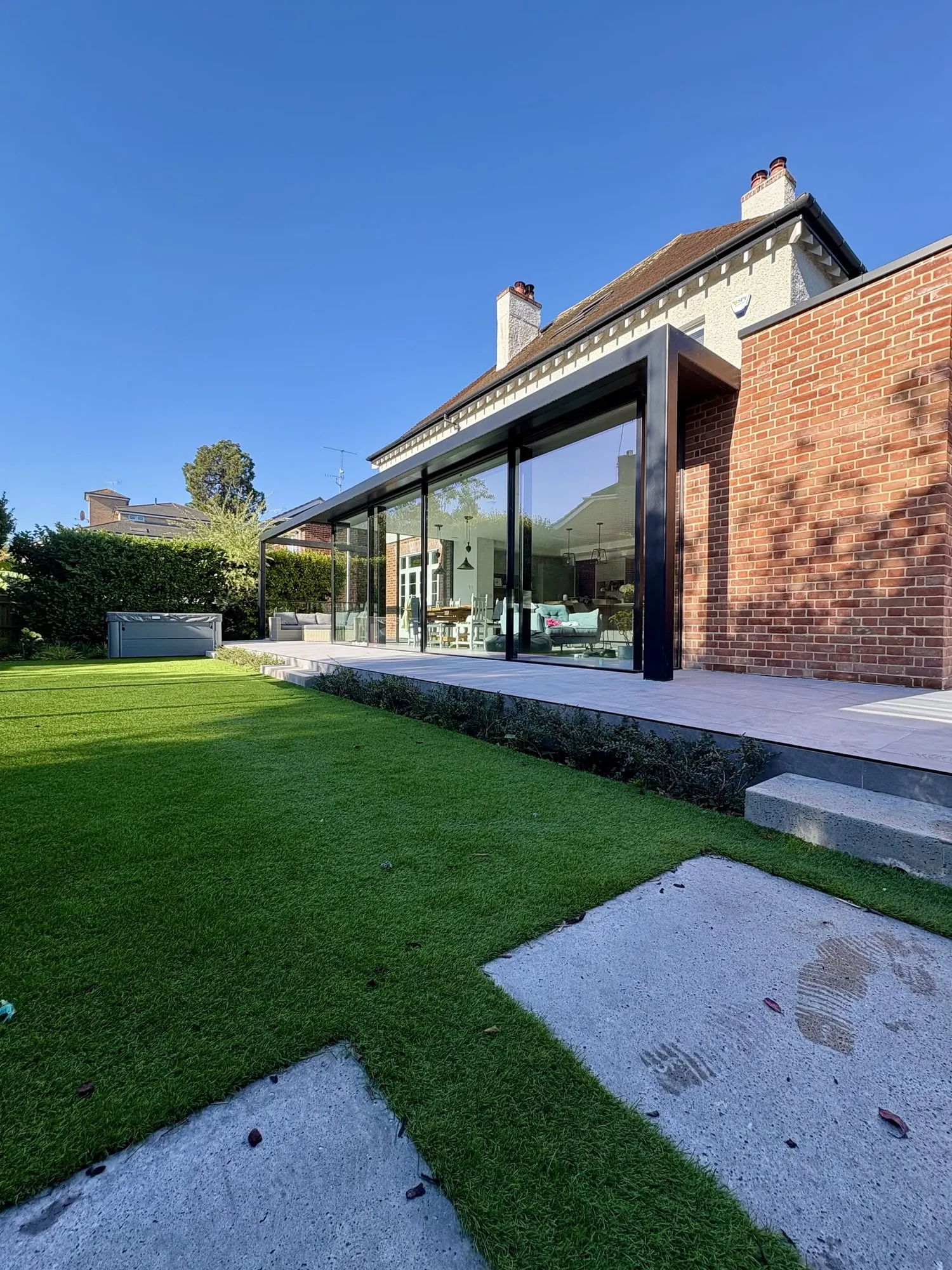 Contemporary brick and glass house in evening light, with a level lawn and stone stepping stones