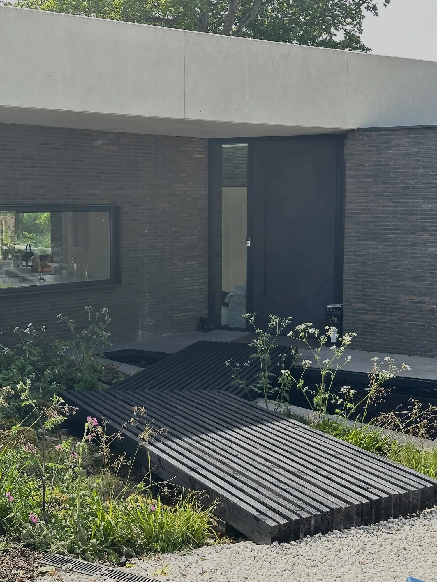 Black rendered contemporary house with a slatted timber path leading to the entrance