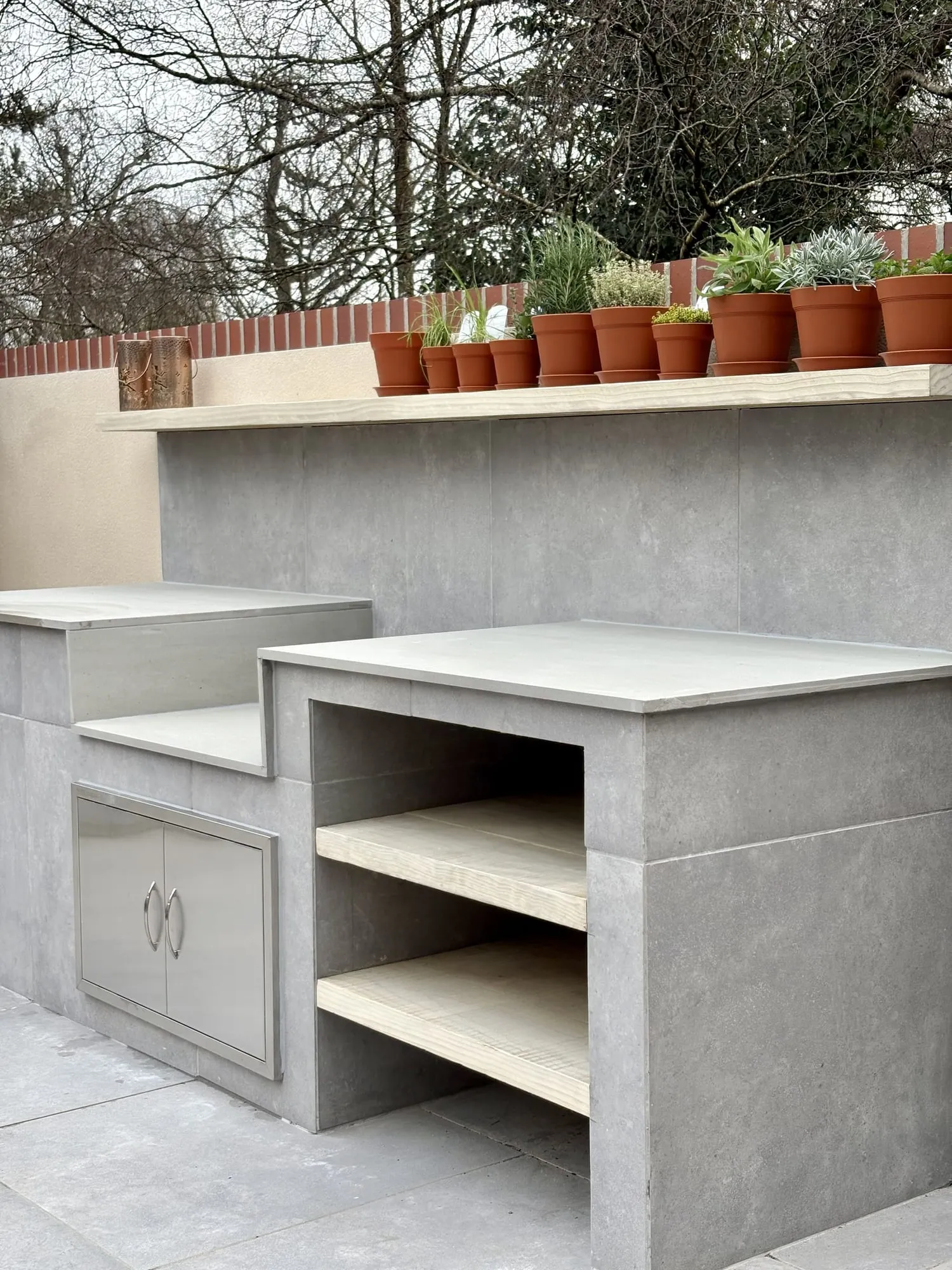 Rendered outdoor kitchen with a concrete worktop and a row of terracotta pots above