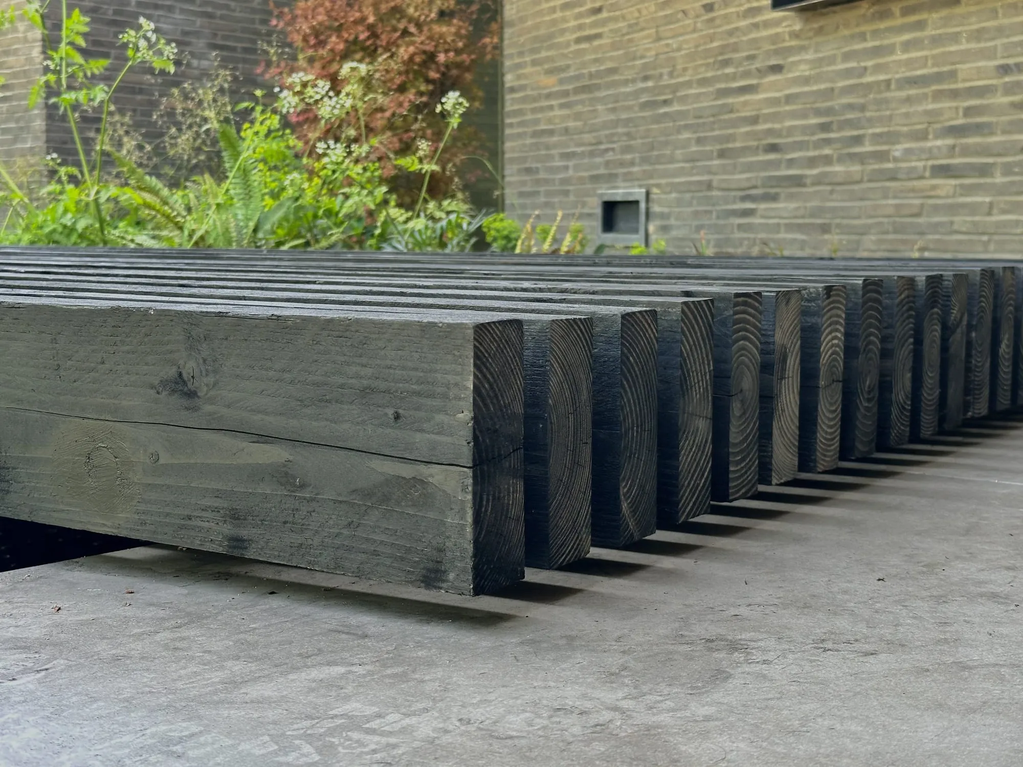 Charred timber sleepers forming a bench against a brick wall
