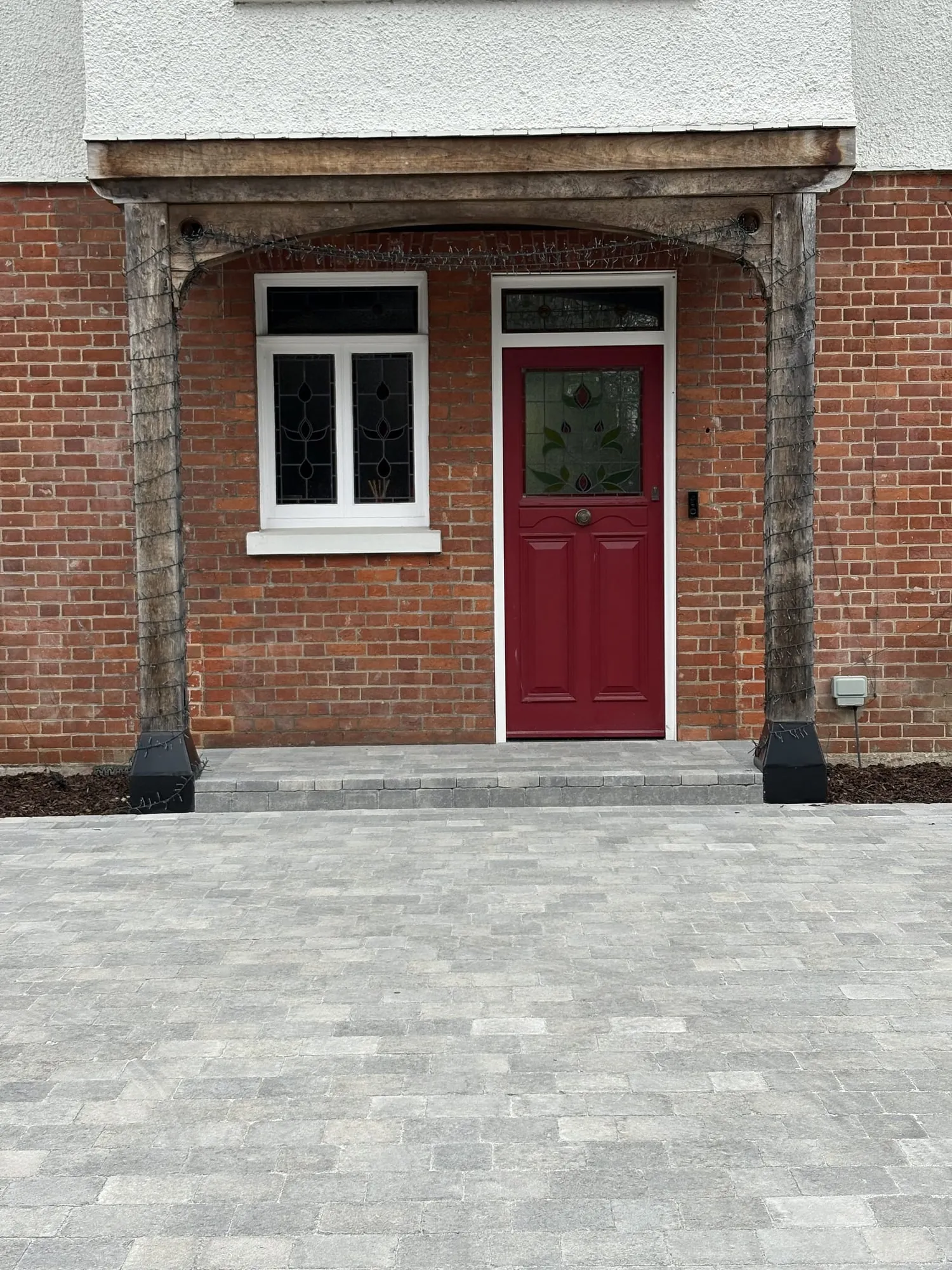 Brick house frontage with a red front door and new block paving