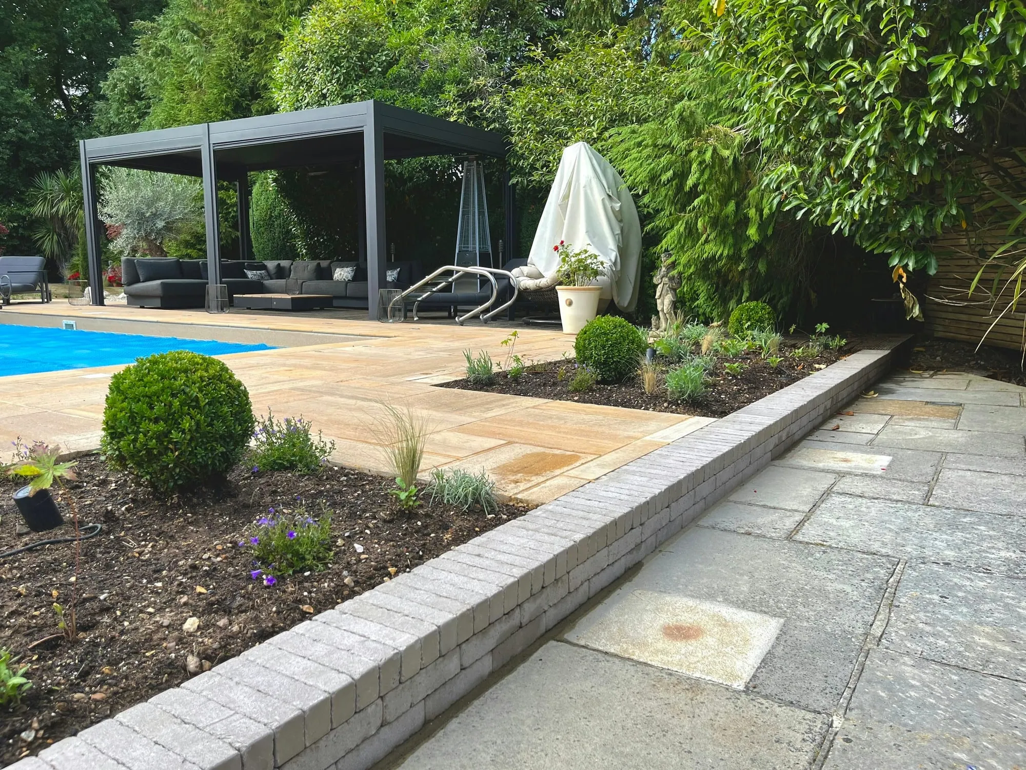 Swimming pool and pergola seen across sandstone paving and planted beds