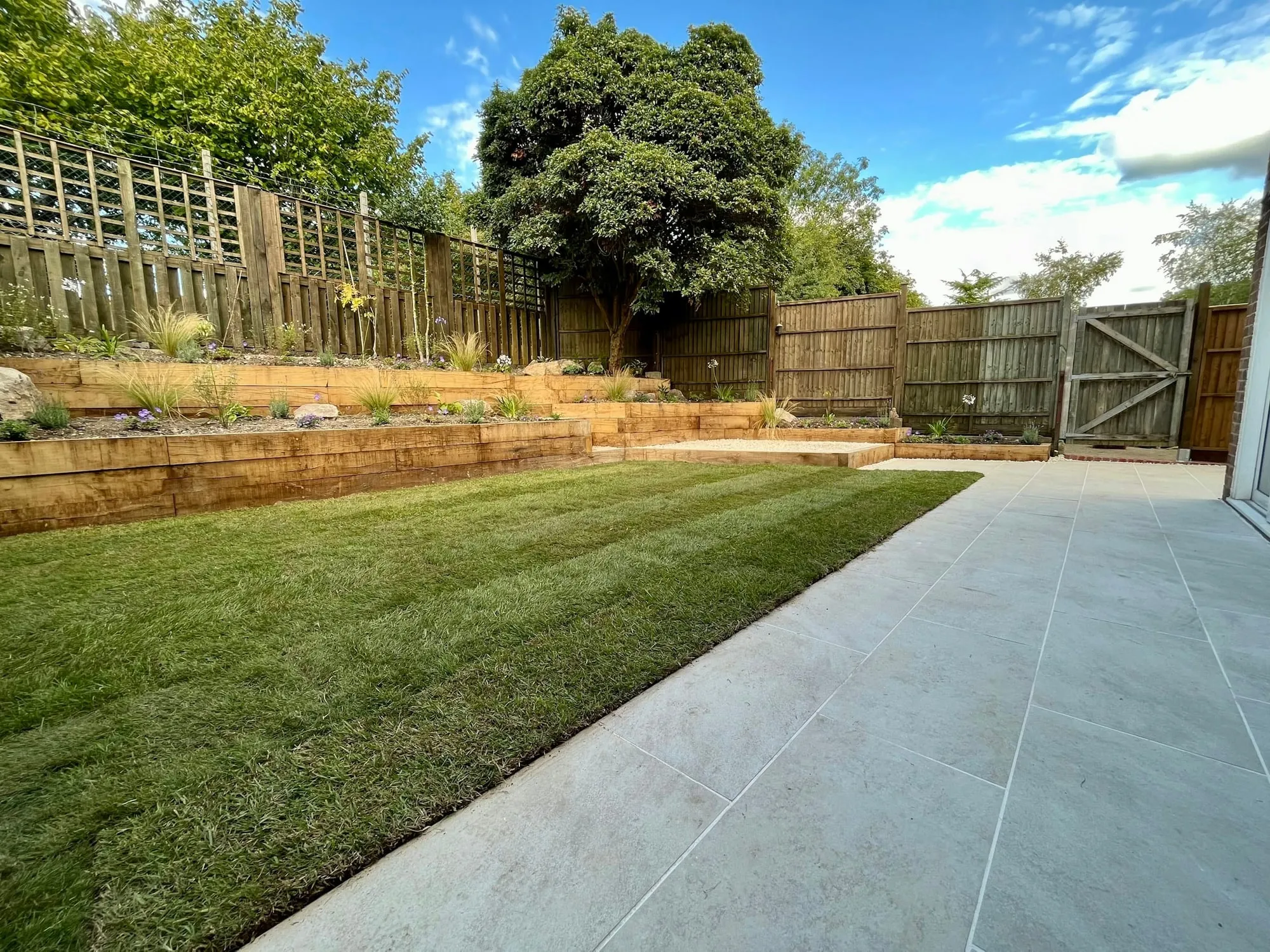 Level lawn beside a wide paved strip, enclosed by close-board fencing