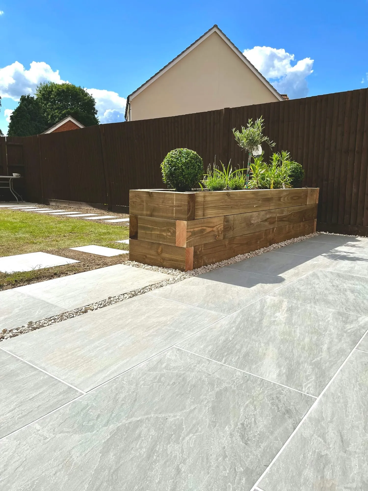 Raised timber planter and stepping stones set into gravel under a blue sky