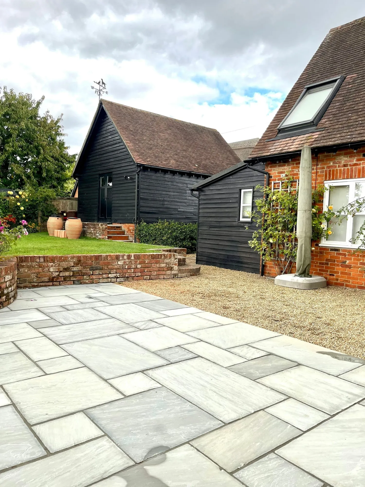 Black timber clad barn with a sandstone paved courtyard