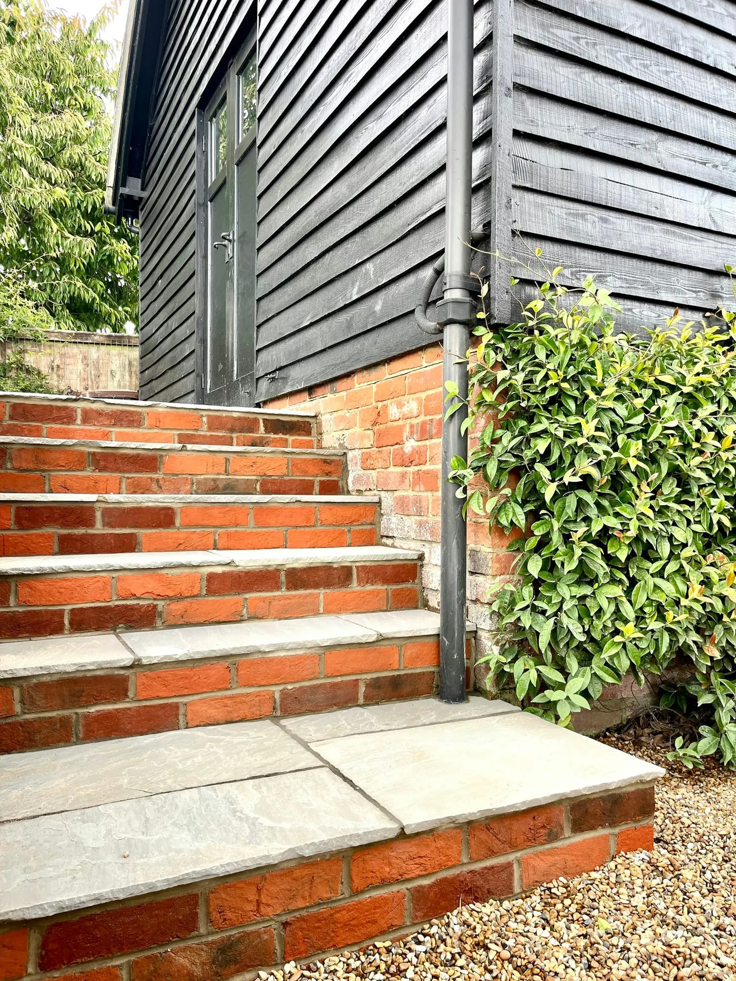 Brick and stone steps rising between planting to a black clad building