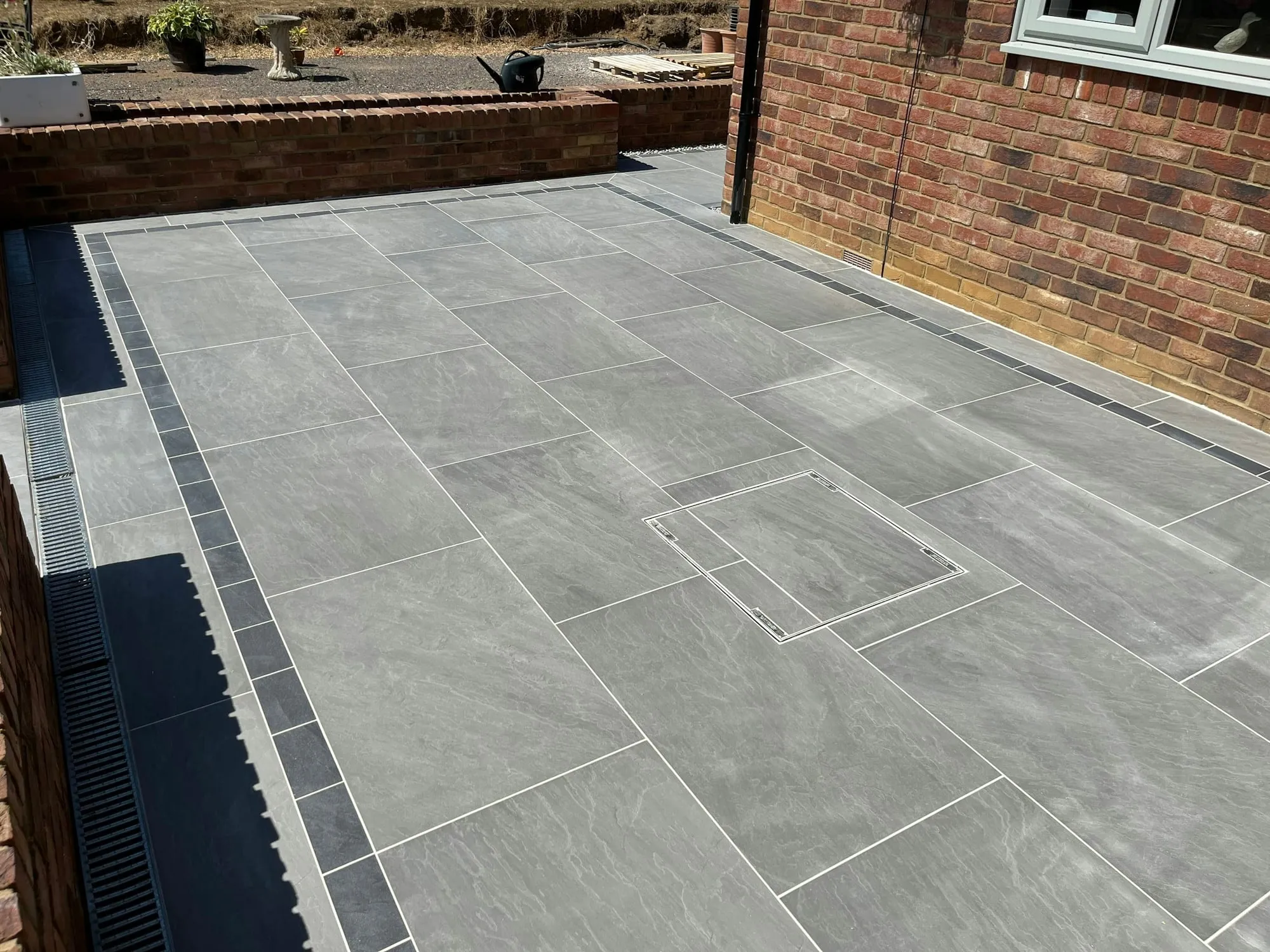 Large grey porcelain patio enclosed by a brick wall