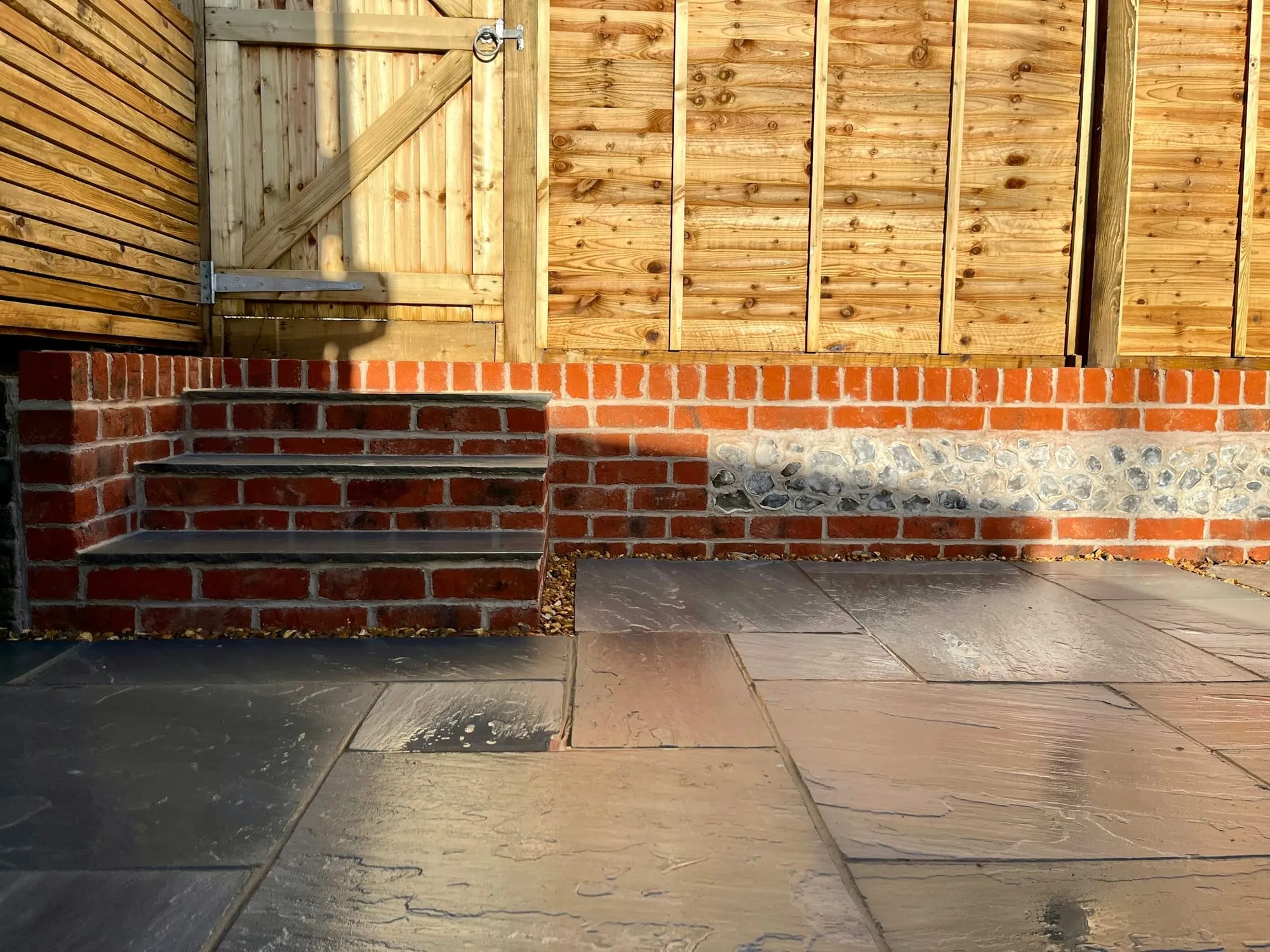 Sandstone paving laid beside a timber fence and a flint wall